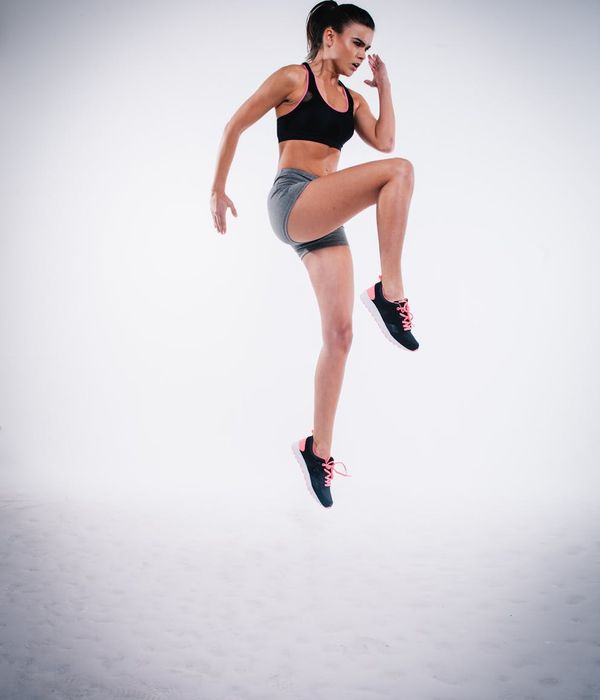 Energetic woman performing a cardio exercise in a modern studio with teal light accents.
